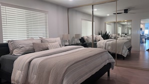 A modern bedroom with a large bed, bedside lamps, a mirror, and a view into the adjacent living area.