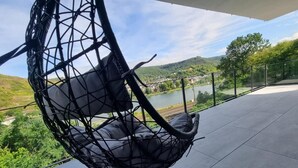 A modern outdoor seating area with a hanging chair, a view of a lake, and a hilly landscape in the background. - Vacation apartment MV Römervilla Loft 3 with a fantastic view of the Moselle in Treis-Karden COC (Treis-Karden)
