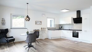 A modern kitchen with white cabinets, a black range hood, and a built-in oven. There is a dining area with a table and chairs, and a bicycle on the wall. - Vacation apartment MV Römervilla Loft 3 with a fantastic view of the Moselle in Treis-Karden COC (Treis-Karden)