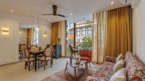 A modern living room with a sofa, dining table, chairs, and a balcony with curtains. - Hidden Gem Luxe Suite w Pool View - 1km to Beach (Candolim)