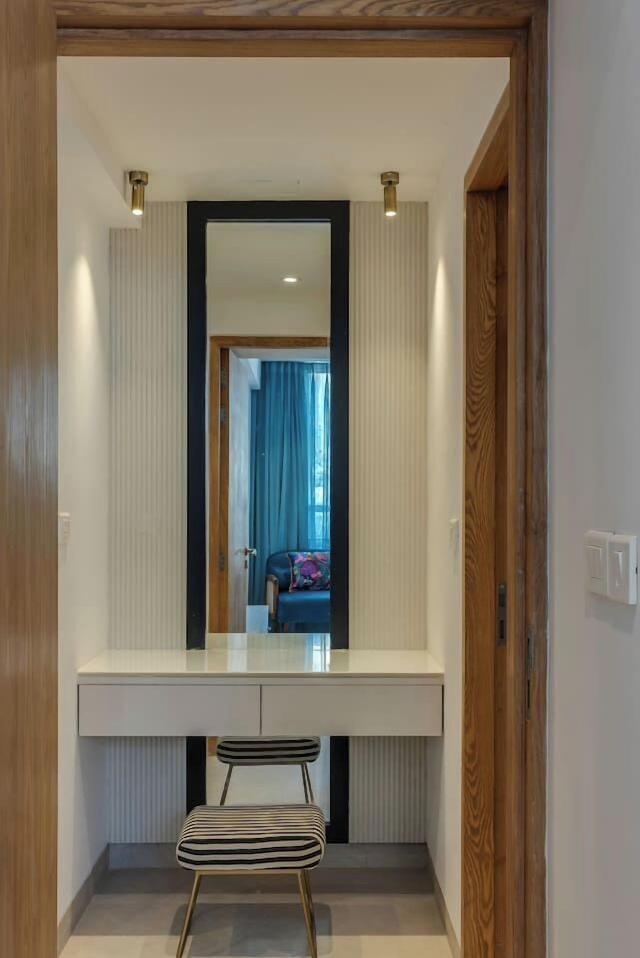 A modern bathroom with a large mirror, a white vanity, a striped chair, and a wooden door frame.