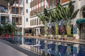 Een modern gebouw met een zwembad, terrasmeubels en tropische planten.