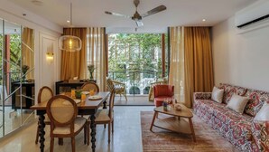 A modern living room with a dining area, large windows, and a ceiling fan. - Hidden Gem Luxe Suite w Pool View - 1km to Beach (Candolim)