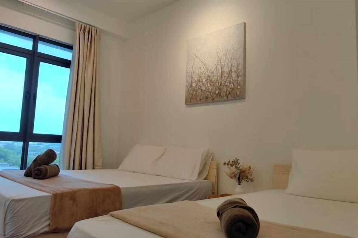 A hotel room with two beds, a window with curtains, a painting on the wall, and a vase with dried flowers.