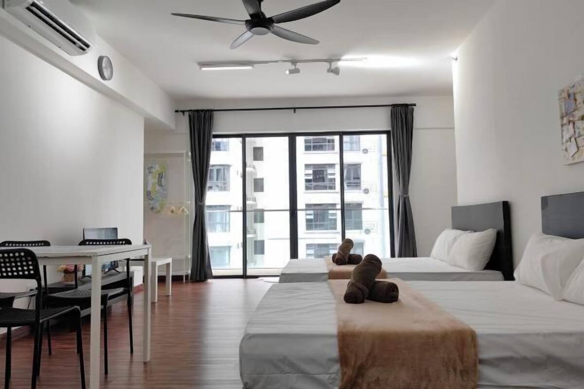 A hotel room with a bed, a desk, and a chair. There is a window with curtains, a ceiling fan, and an air conditioning unit.