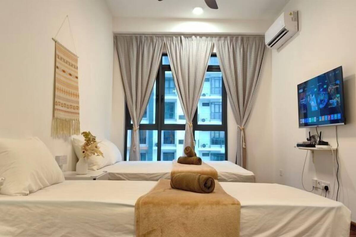 A hotel room with two beds, a TV, an air conditioner, and a window with curtains.