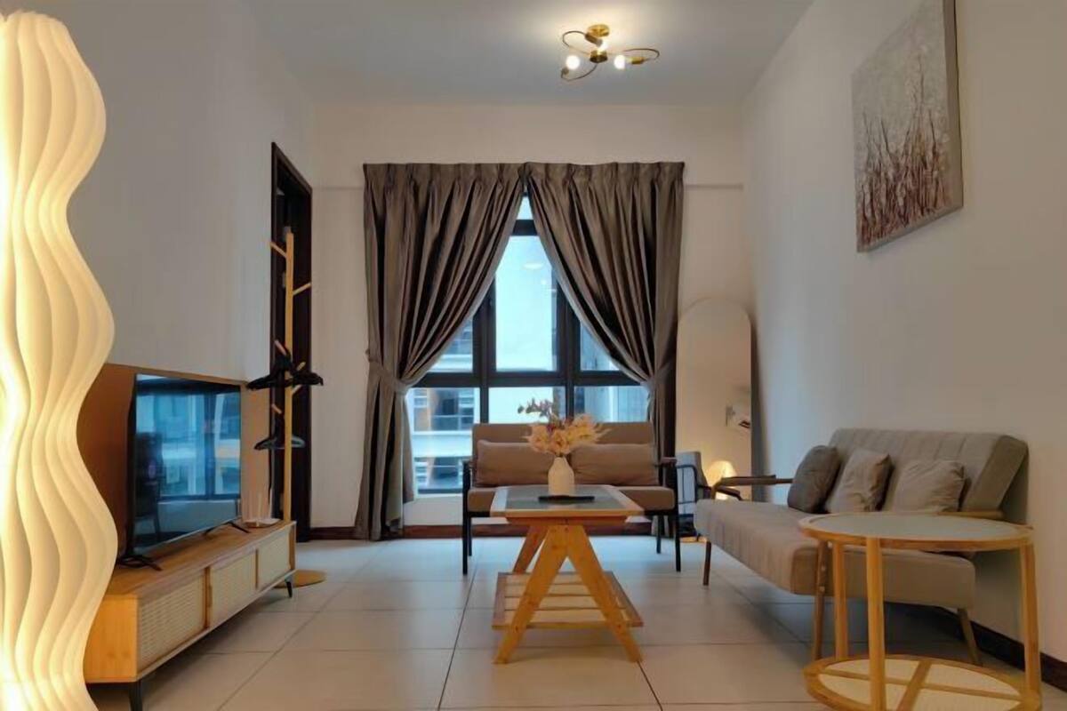 A modern living room with a TV, sofa, coffee table, and a large window with curtains.