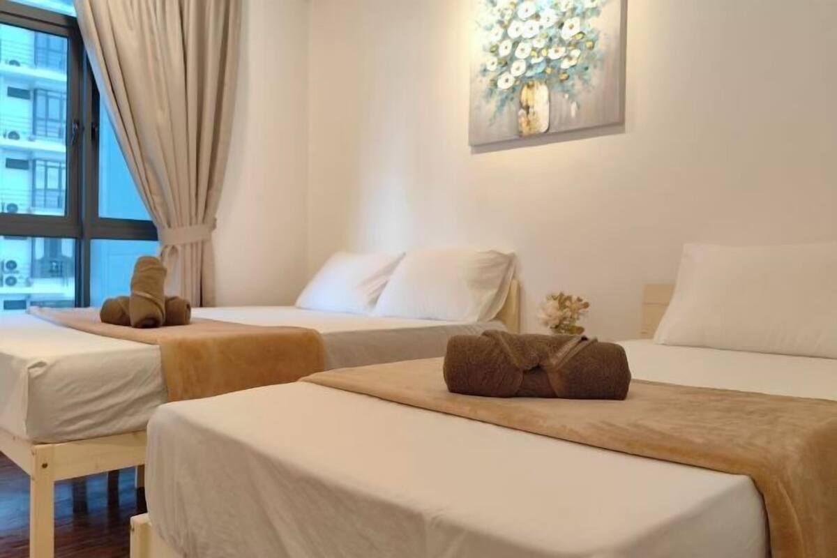 A hotel room with two beds, a window with curtains, a painting on the wall, and a small plant on the bedside table.