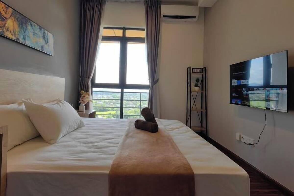 A hotel room with a bed, a TV, a window with curtains, and a painting on the wall.