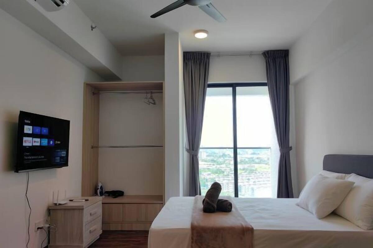 A hotel room with a bed, a TV mounted on the wall, a wardrobe, and a window with curtains.