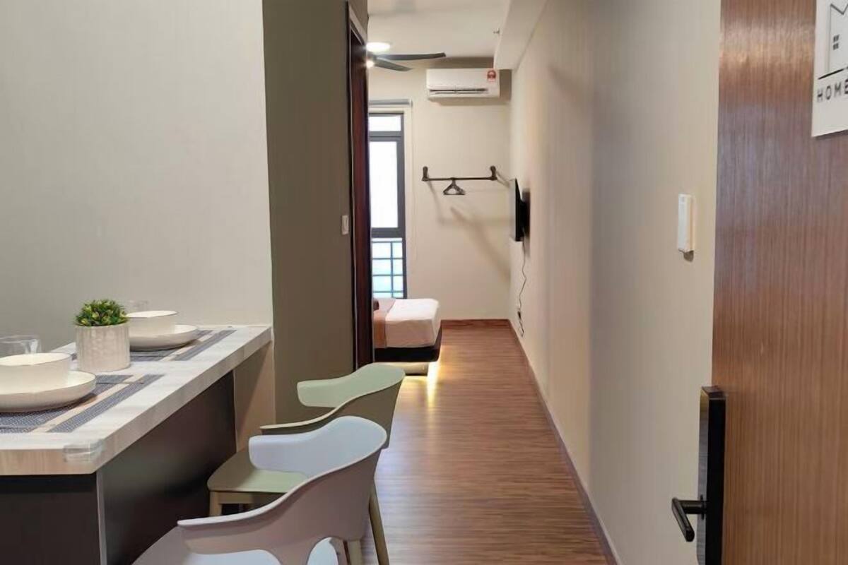 A modern hotel room with a wooden floor, a small seating area with chairs, a bedside table, and a bed.
