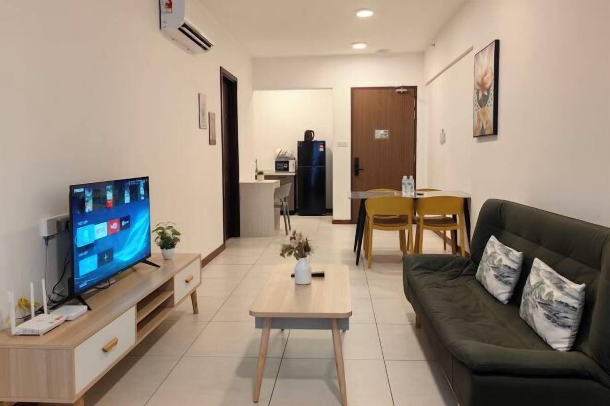 A living room with a TV, a sofa, a coffee table, and a dining area.