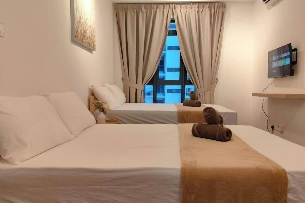 A hotel room with two beds, a TV on the wall, and a window with curtains.