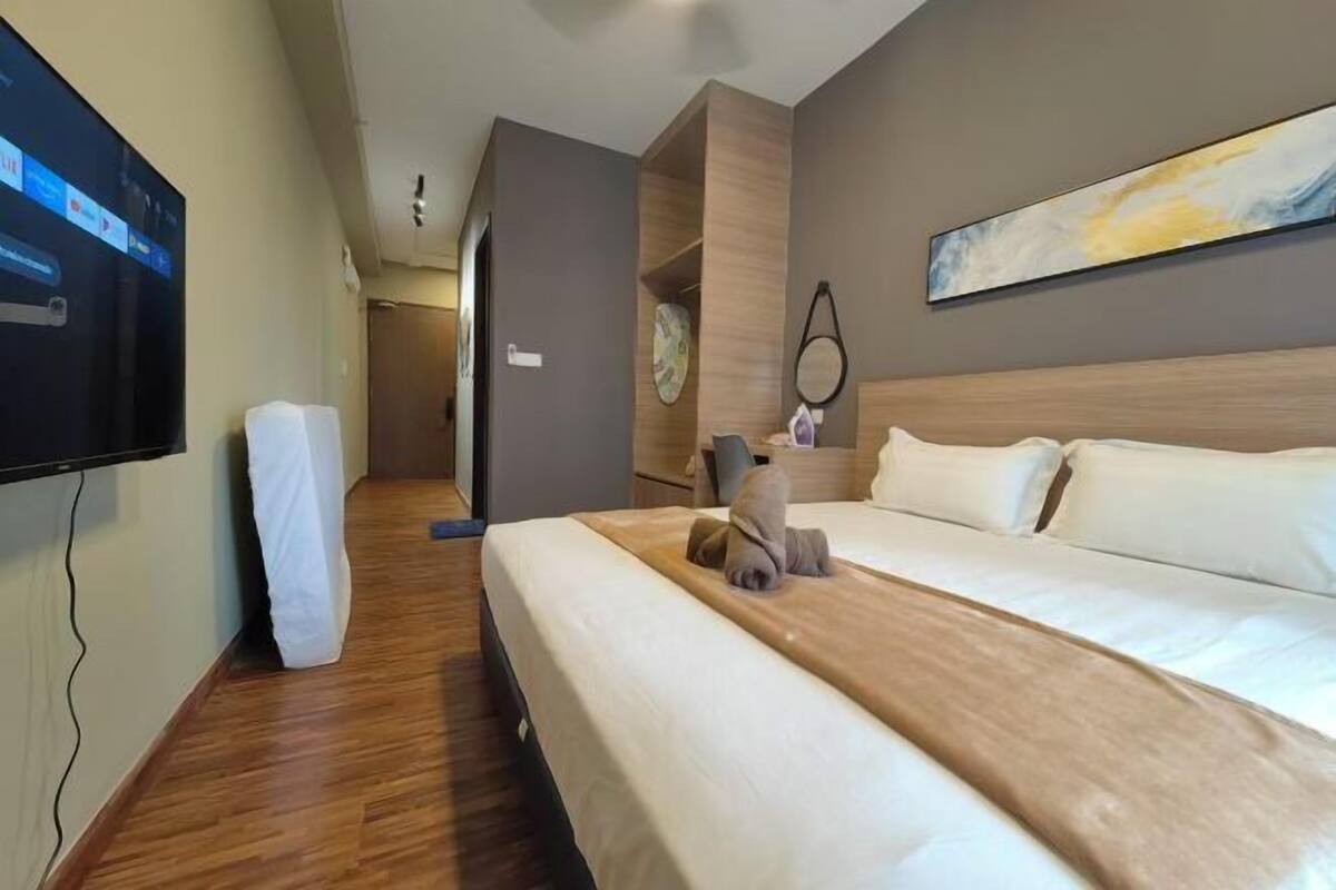 A hotel room with a bed, a TV mounted on the wall, a painting above the bed, and a wooden floor.