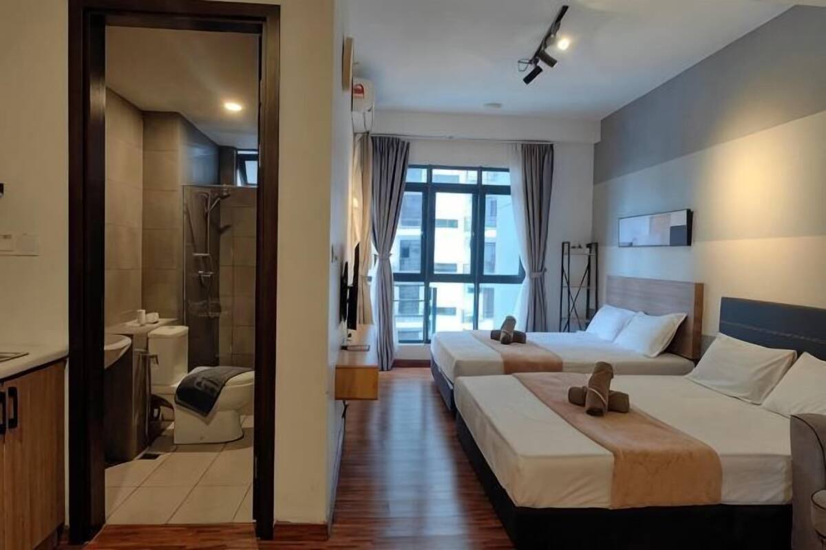 A hotel room with two beds, a shower, a window with curtains, and a view of the city.