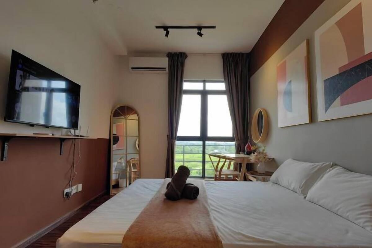 A hotel room with a bed, a flat-screen TV, a window with curtains, and a view of the outdoors.