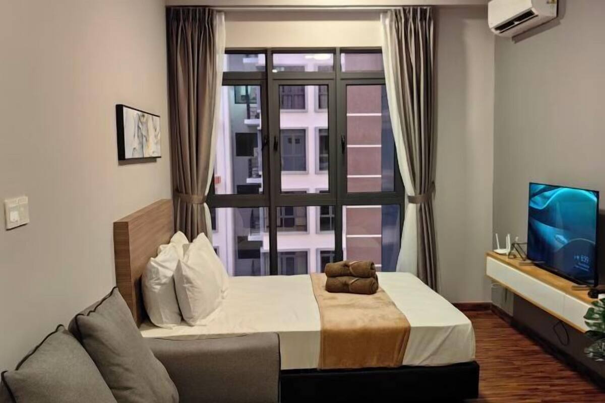 A hotel room with a bed, a TV, and a window with curtains.