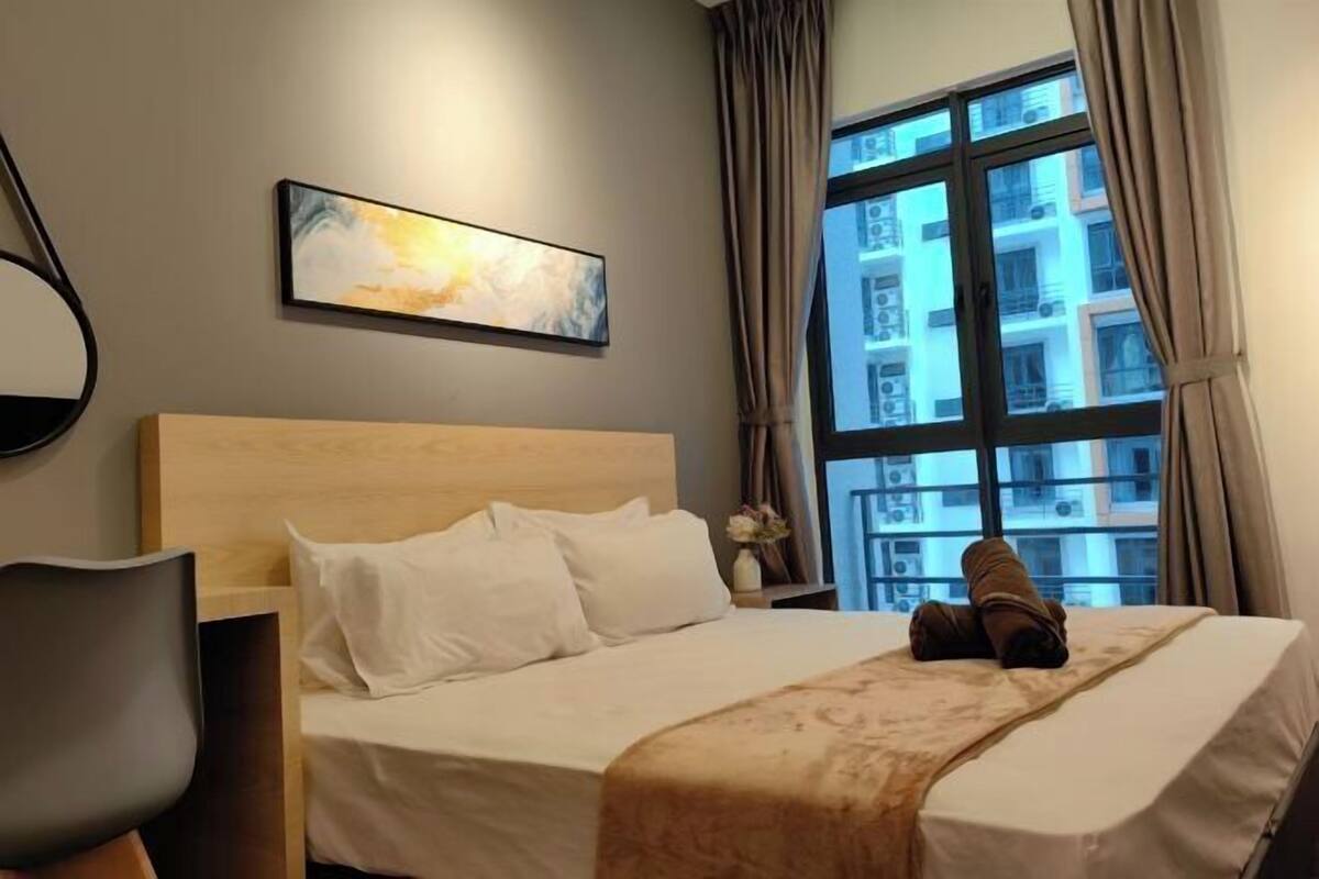 A hotel room with a bed, a chair, a window with curtains, and a painting on the wall.