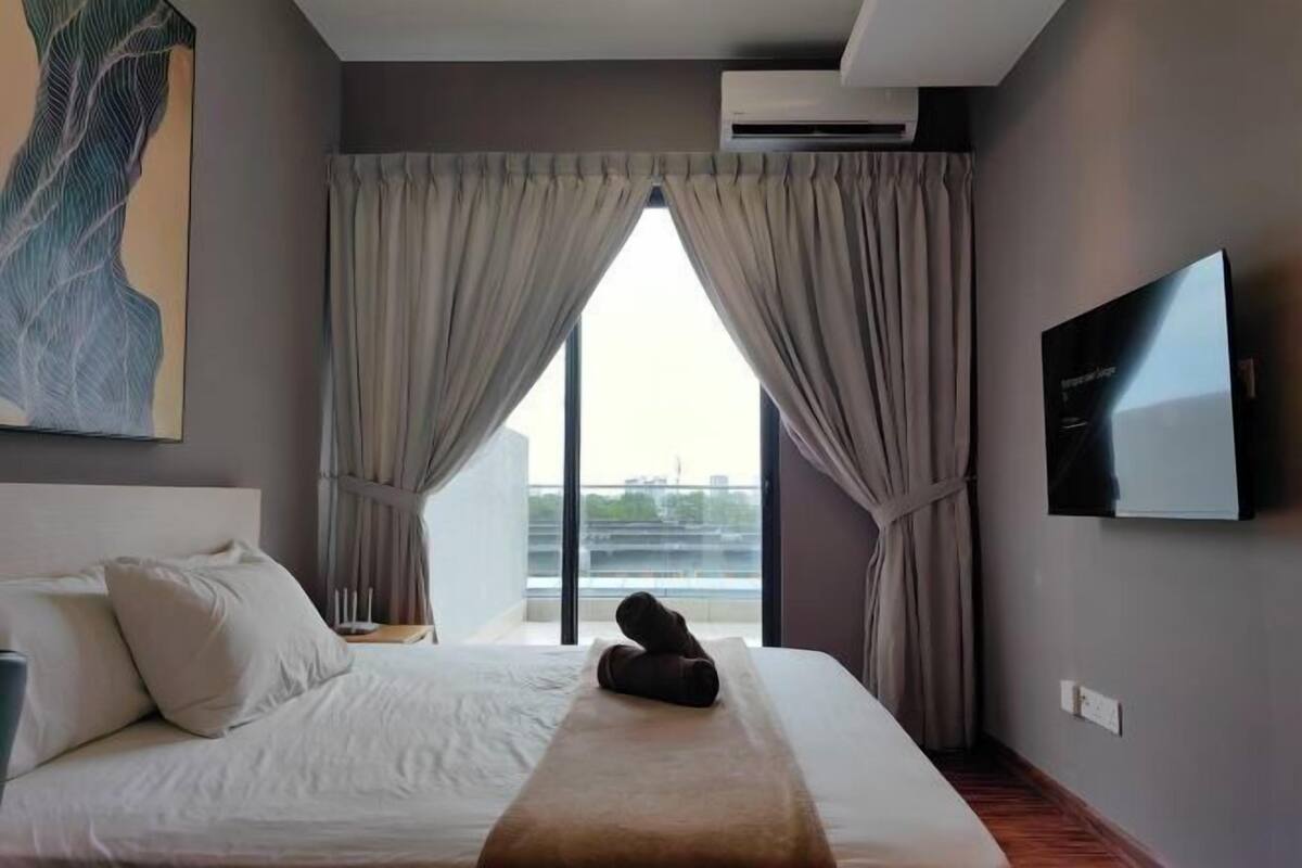 A hotel room with a bed, curtains, a TV, and a view of the outside.