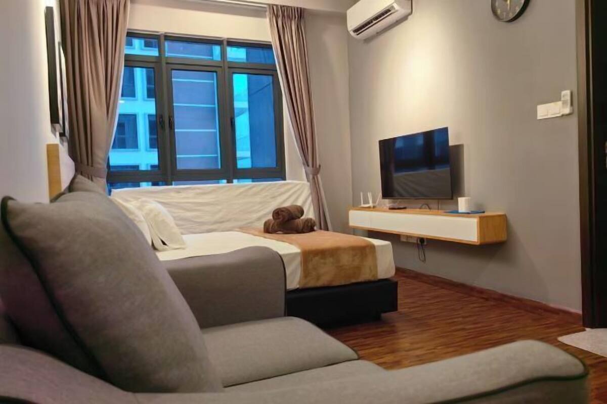 A modern hotel room with a bed, a sofa, a TV, and a window with curtains.