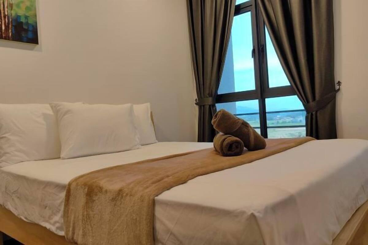 A hotel room with a bed, a window with curtains, and a view of the sea.