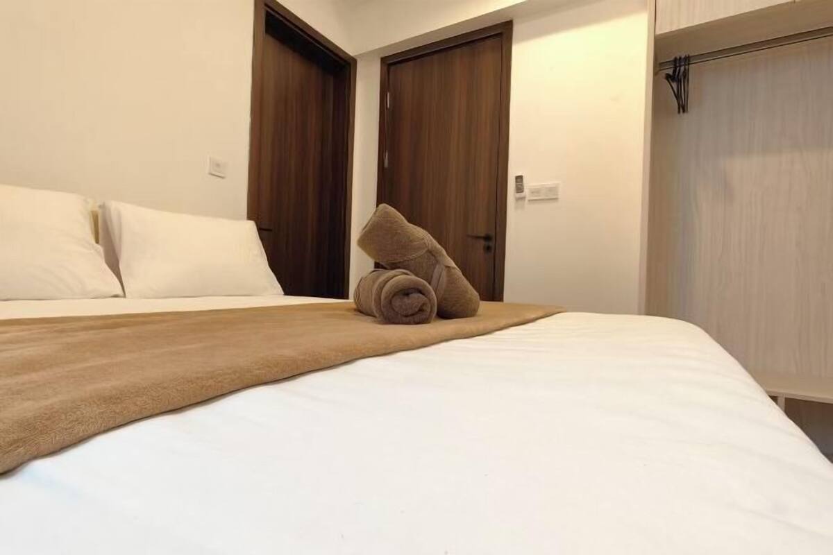 A neatly made bed with a brown blanket and rolled towels, two wooden doors, and a light-colored wall.