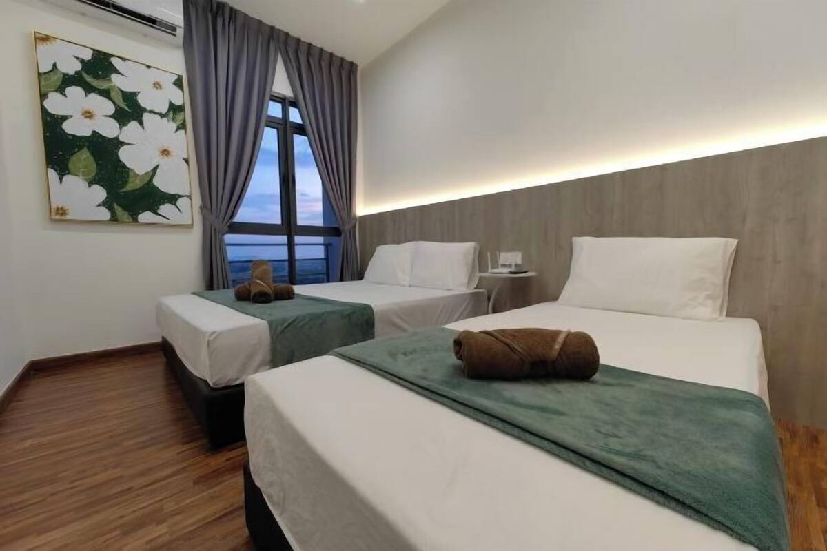 A hotel room with two beds, a window with curtains, a painting on the wall, and a nightstand with a lamp.
