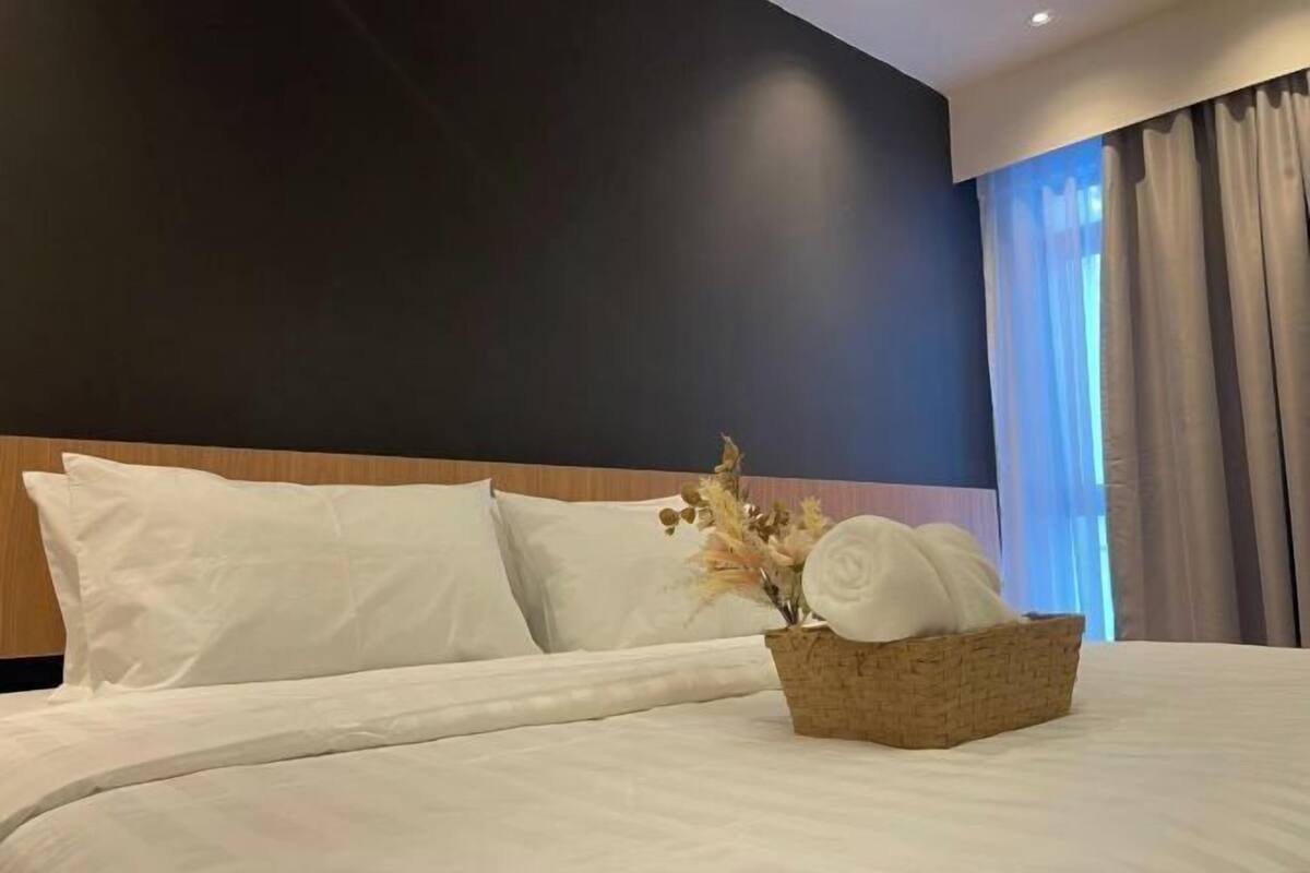 A neatly made bed with white linens, a headboard, and a basket with rolled towels and dried flowers.