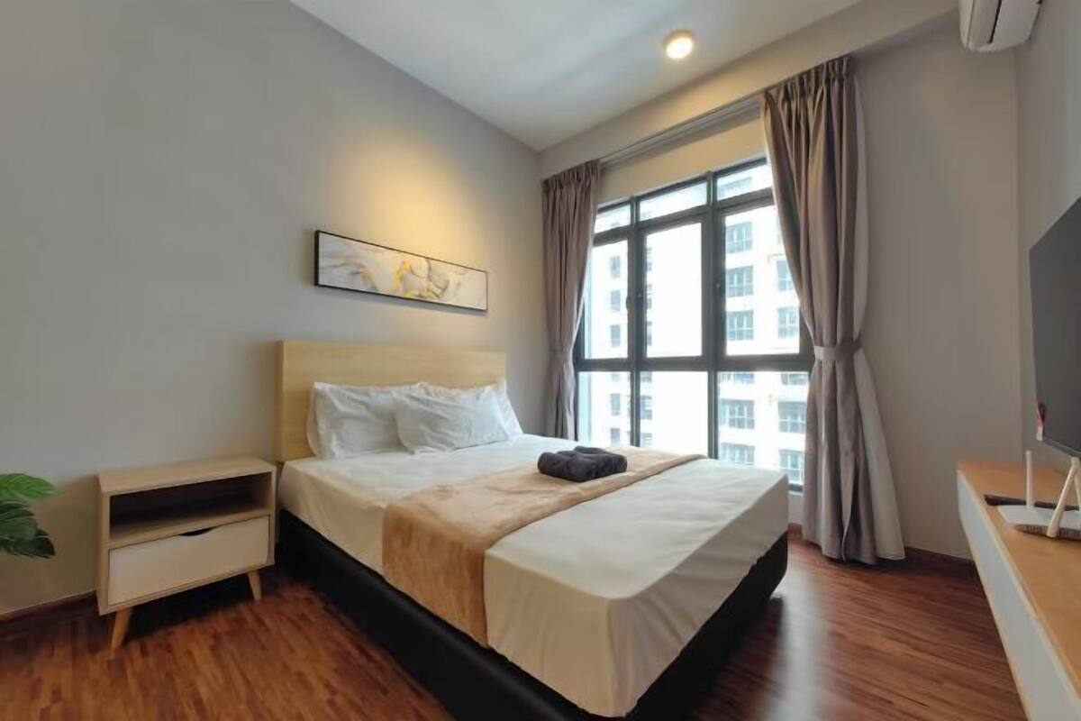 A hotel room with a bed, bedside table, TV, and a window with curtains.