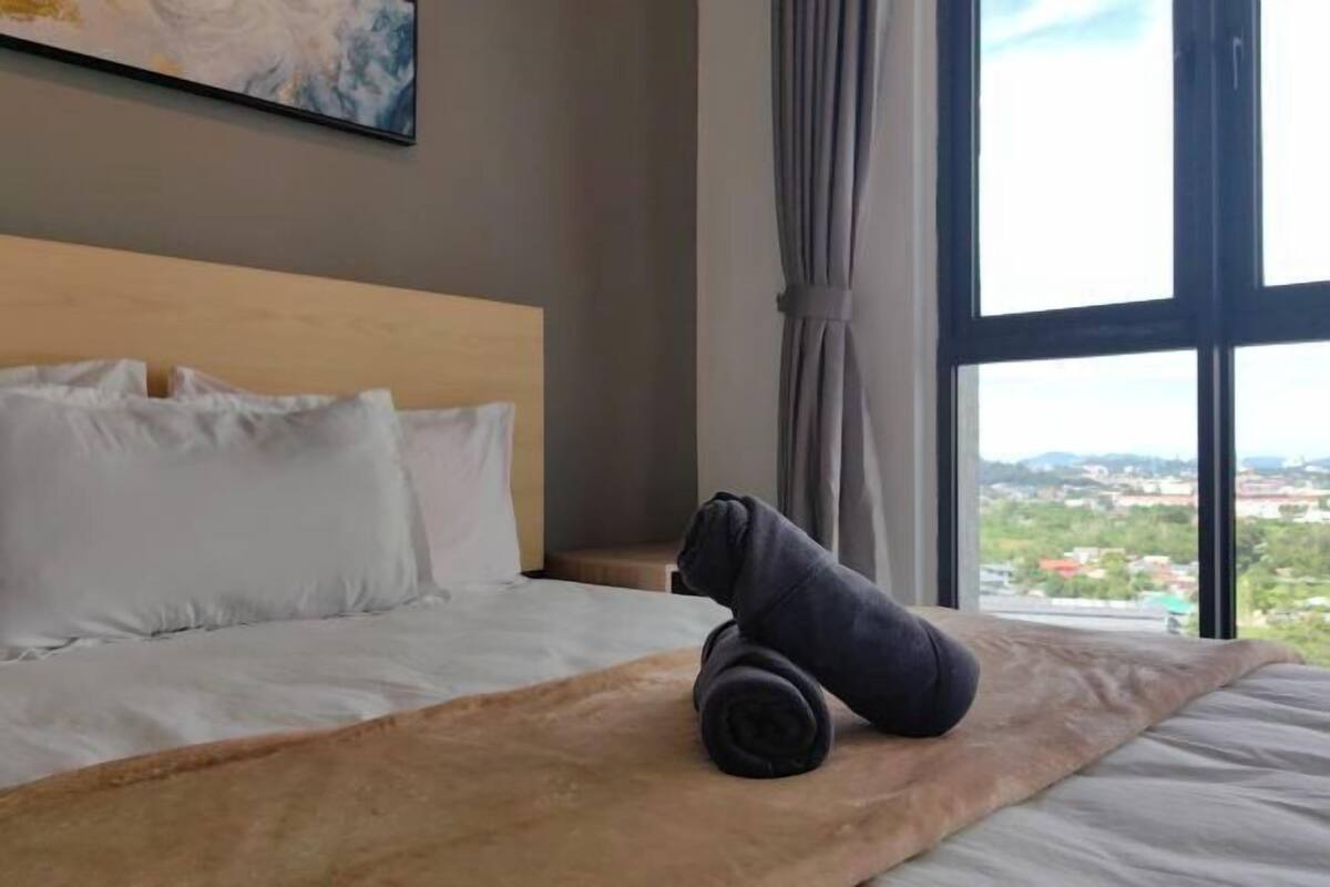 A hotel room with a bed, a view through a large window, and a painting on the wall.