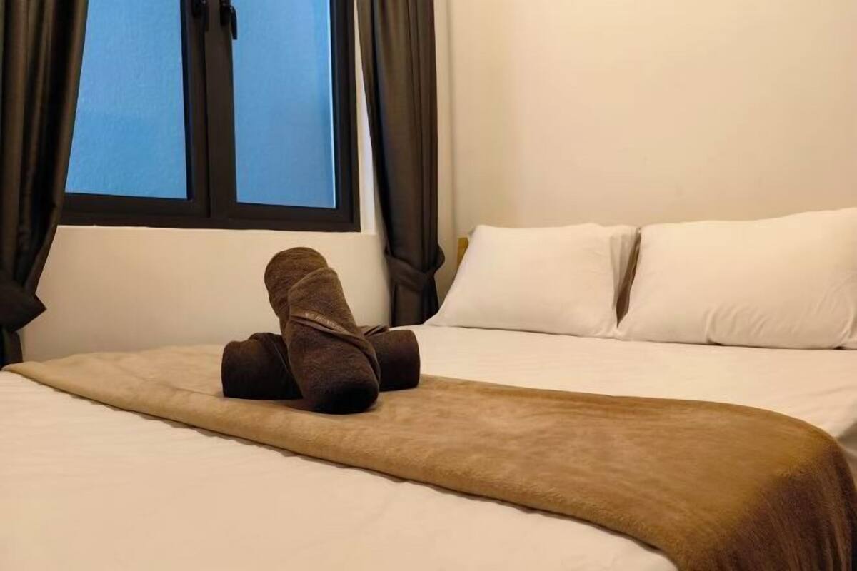 A hotel room with a bed, a window with curtains, and a blanket.