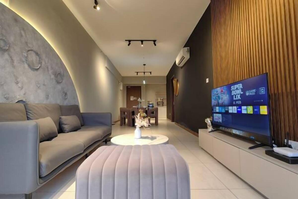 A modern living room with a sofa, ottoman, and a flat-screen TV displaying the Super Bowl LIX.