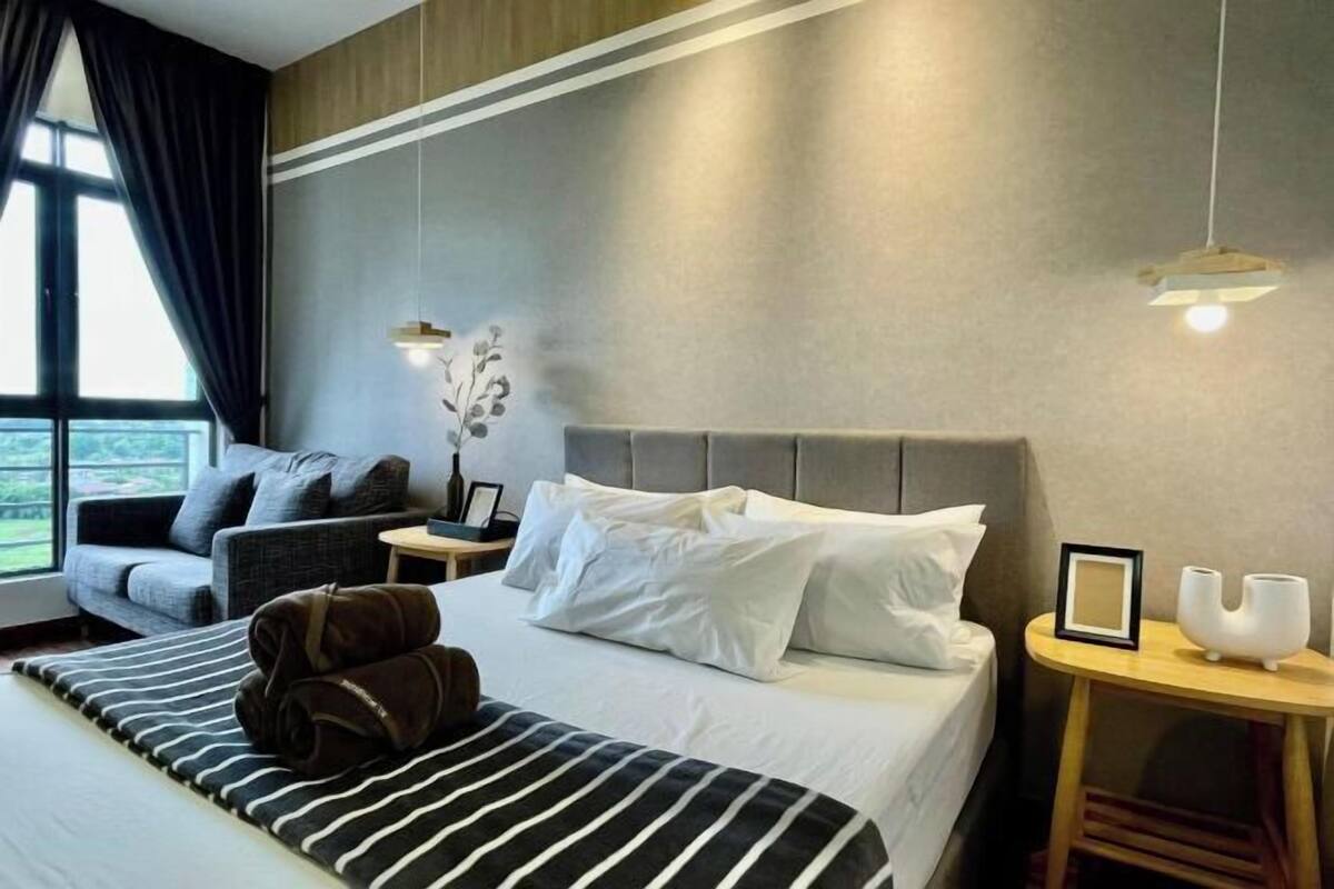 A hotel room with a bed, a sofa, a nightstand, and a window with curtains.