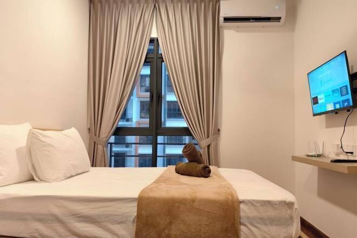A hotel room with a bed, a TV on the wall, and a window with curtains.