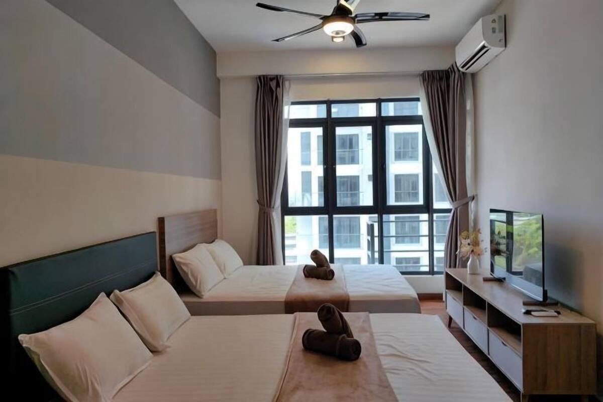A hotel room with two beds, a ceiling fan, a TV, and a large window with curtains.