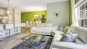A modern living room with a white sofa, a glass coffee table, and a dining area with white chairs.