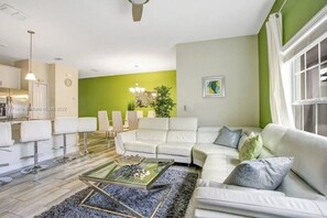 A modern living room with a white sofa, a glass coffee table, and a dining area with white chairs.