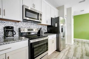 Una cocina con armarios blancos, un refrigerador negro, un microondas, una cafetera y una estufa.