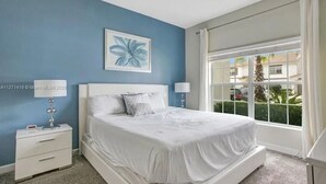 A bedroom with a bed, two bedside tables, a window with curtains, and a wall painting.