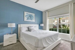 A bedroom with a bed, two bedside tables, a window with curtains, and a wall painting.