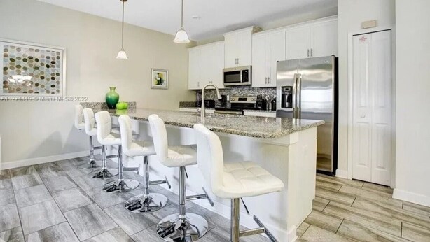 A modern kitchen with white bar stools, a stainless steel refrigerator, and a granite countertop.