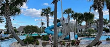 Zona de piscina con tobogán de agua, palmeras y cielo despejado.
