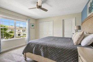 A bedroom with a bed, a ceiling fan, a window with curtains, and a view of a building outside.