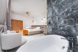 A modern bedroom with a large white bathtub, a bed with a wooden headboard, and a ceiling fan.