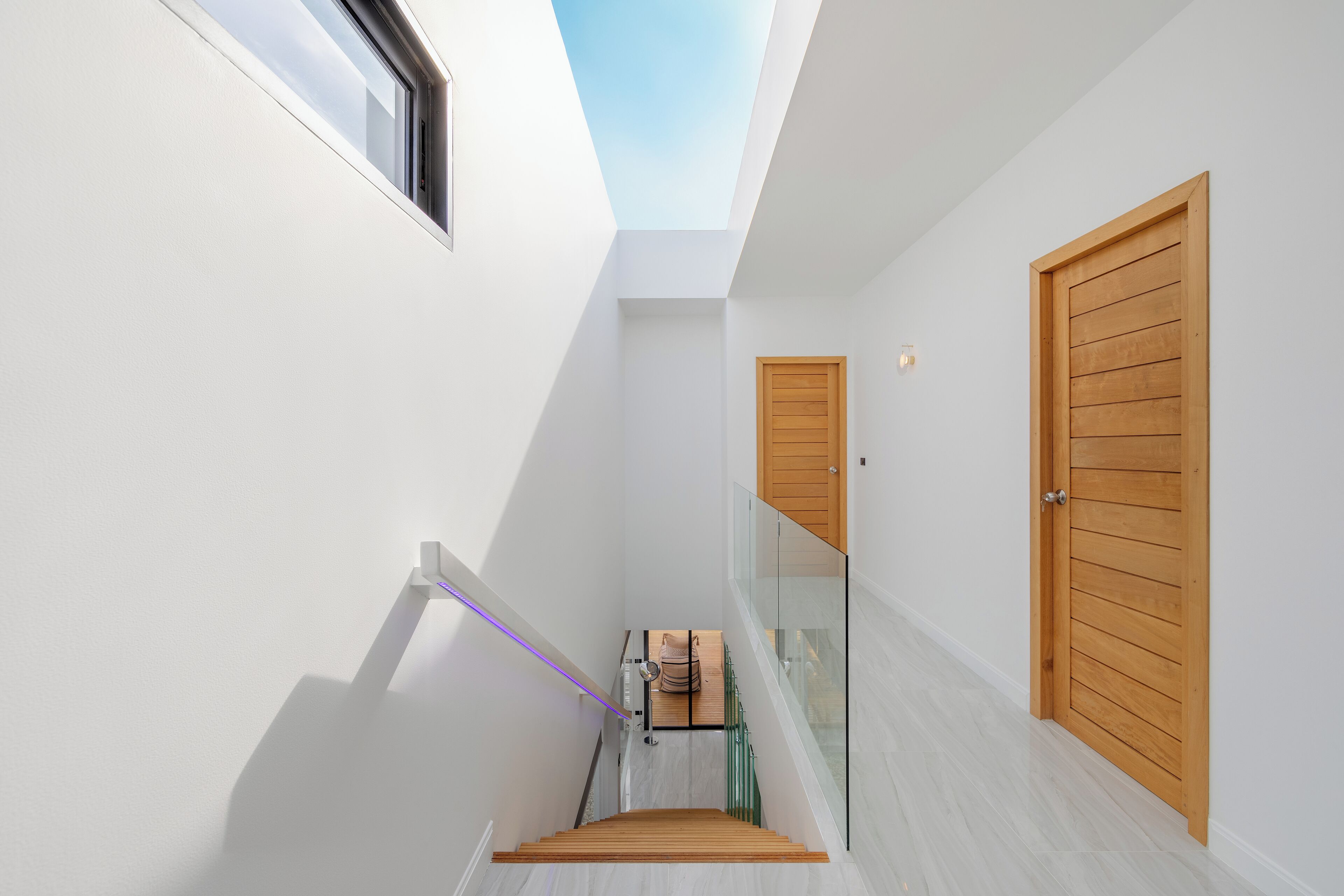 A narrow hallway with a skylight, wooden doors, and a glass railing.