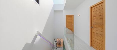 A narrow hallway with a skylight, wooden doors, and a glass railing.