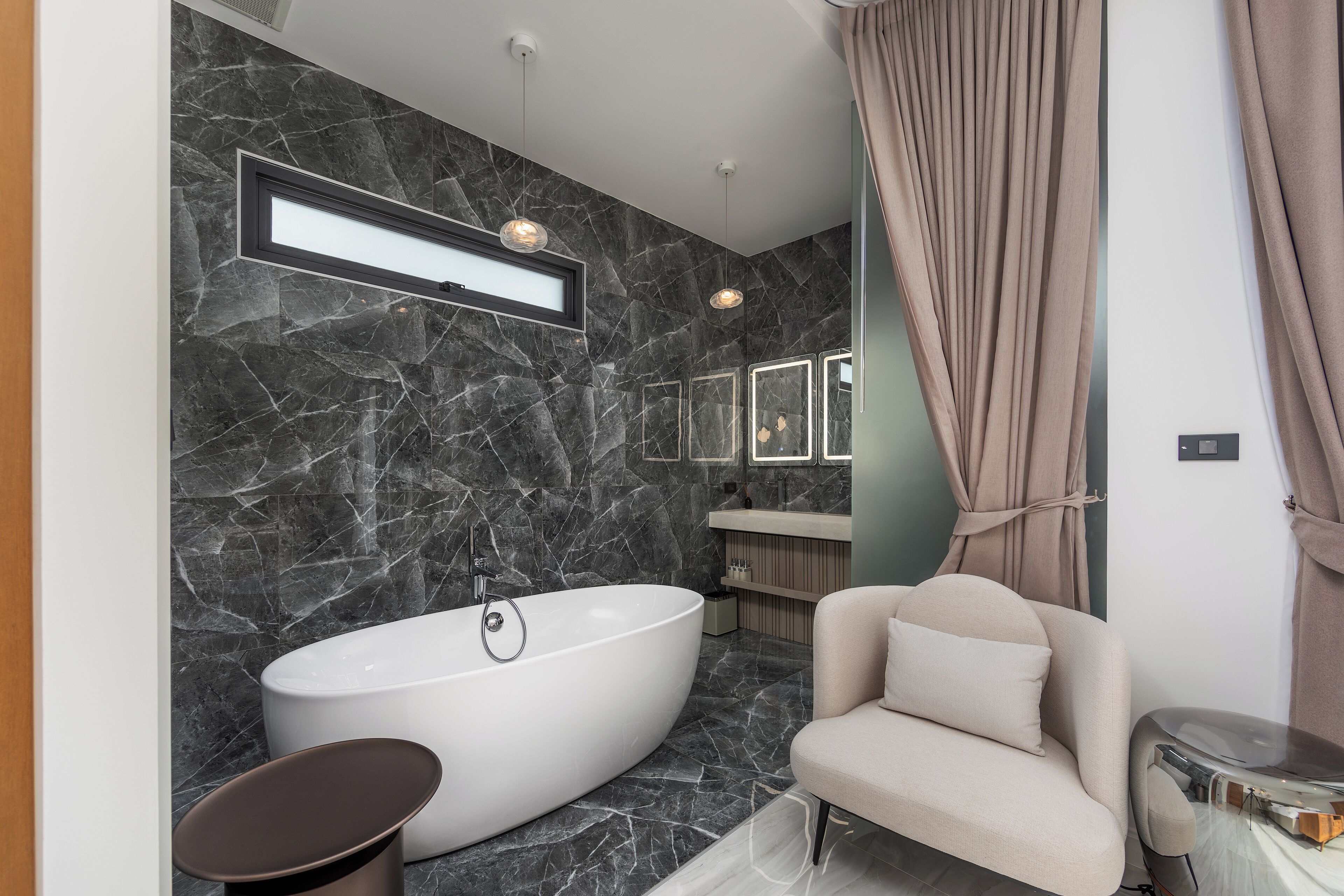 A modern bathroom with a freestanding bathtub, a vanity, and a sofa.