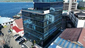 A modern multi-story building with a glass facade, located near a body of water. - Semporna Lighthouse Hotel (Semporna)