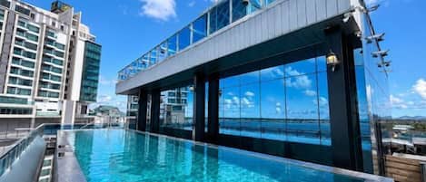 A rooftop infinity pool with a clear view of the ocean and surrounding buildings.