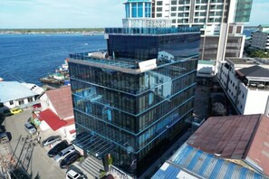 A multi-story building with a glass facade, adjacent to a body of water, with a parking area in front. - Semporna Lighthouse Hotel (Semporna)